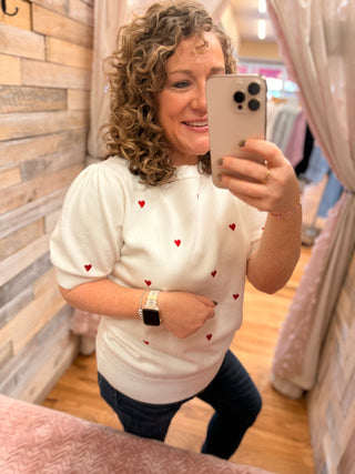 Woman taking a mirror selfie wearing a white shirt with red heart patterns.