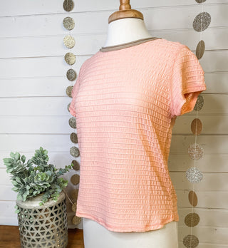 a peach short sleeve ruched style top with a taupe colored neckline