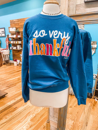 A teal colored sweatshirt that says so very thankful in a colorful print